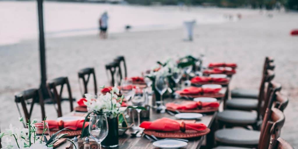 Ein gemütlicher Tisch am Strand mit roten Gedecken.