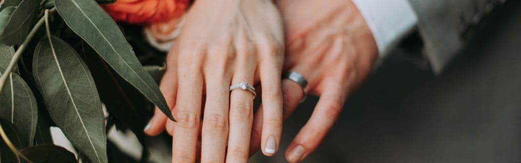 Eine Hochzeit im Bild: Die Hände einer Braut und eines Bräutigams halten den Ehering.