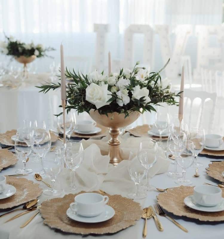 Ein Tischgedeck in Weiß und Gold mit weißen Blumen.